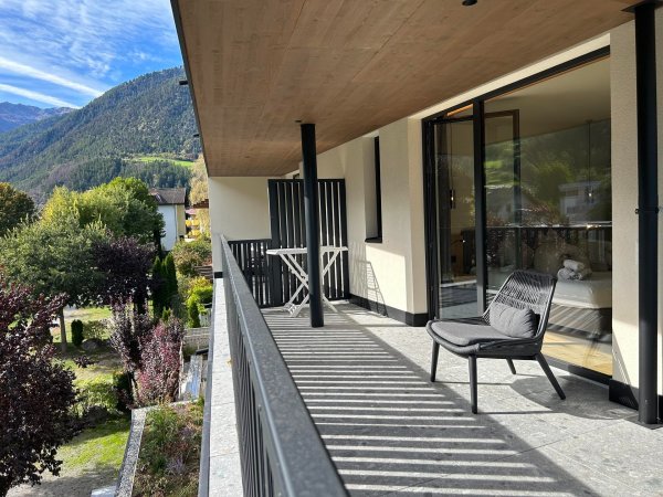 Balcone con sedie, vista su un giardino e montagne verdi.