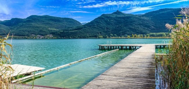 Molo in legno su lago con montagne sullo sfondo.