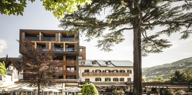 Edificio moderno con balconi in legno accanto a struttura tradizionale, alberi intorno.