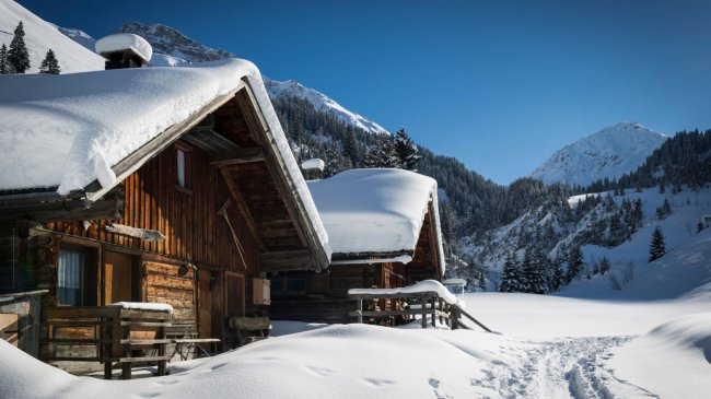 Chalet in legno coperti di neve, con montagna sullo sfondo.