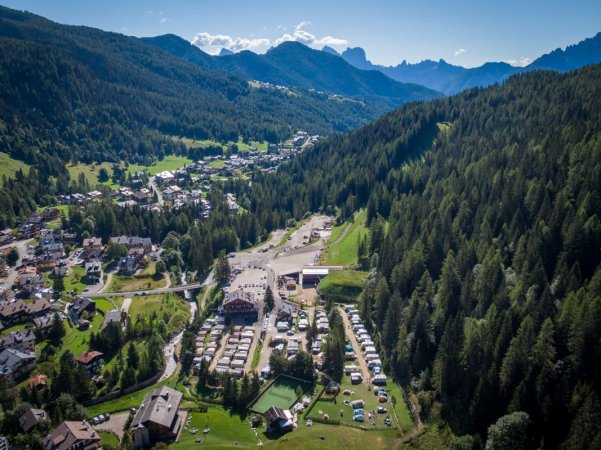 Villaggio con case e foresta vista dall'alto, circondato da montagne.