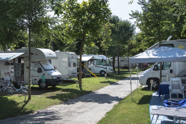 Area campeggio con camper parcheggiati su prato, alberi e un sentiero al centro.