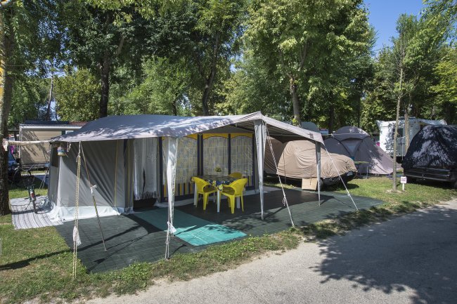 Area campeggio con grandi tende, sedie gialle e tavolo sotto un telo.
