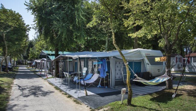 Camper con veranda attrezzata e amaca tra gli alberi lungo un sentiero.