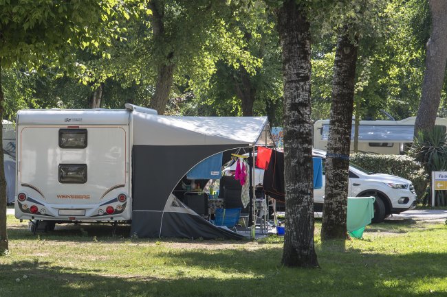 Una roulotte con tenda montata in un campeggio tra alberi.