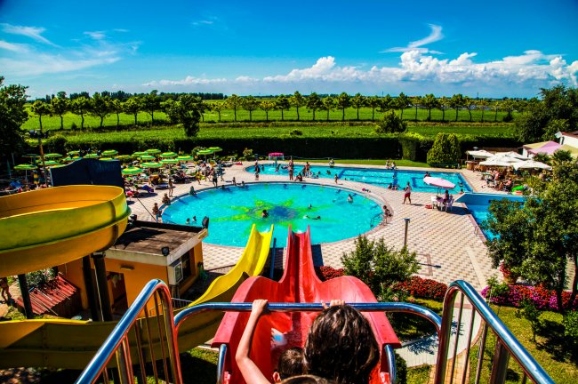 Piscina all'aperto con scivoli colorati e prati verdi intorno.