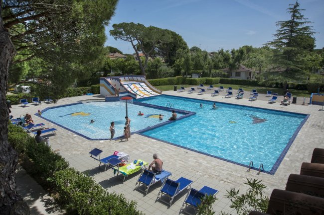 Piscina con lettini, scivolo e alberi intorno in un'area residenziale.