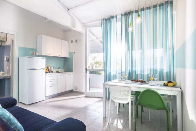 Cucina moderna con tavolo bianco, sedie colorate e tende a righe blu.