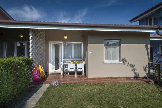 Casa con veranda, prato, tavolo e sedie. Gonfiabili colorati a lato.