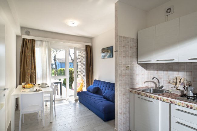 Cucina e soggiorno con divano blu, tavolo apparecchiato e accesso al giardino.