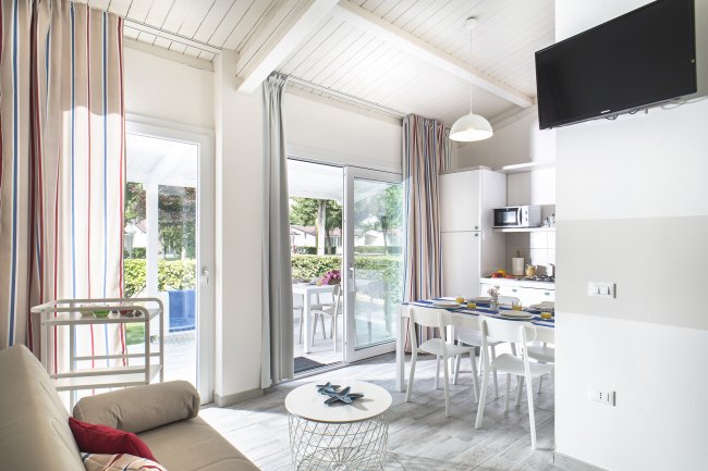 Interno di una casa con divano, tavolo da pranzo, cucina moderna e porte-finestre.