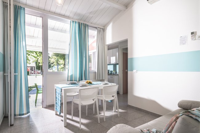 Sala da pranzo luminosa con tavolo bianco e sedie, tende blu e bianche, e vista sul giardino.