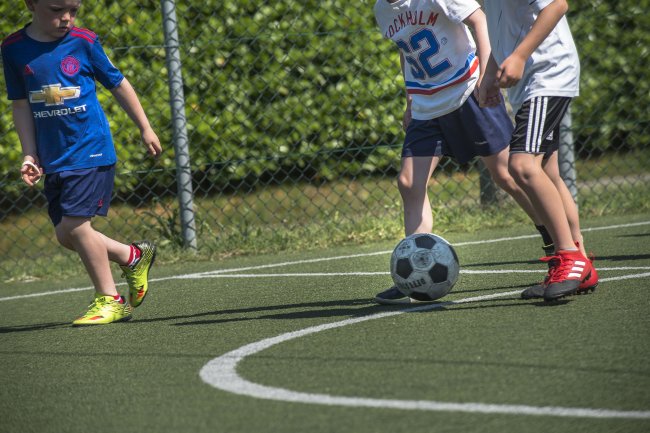 Bambini che giocano a calcio su un campo erboso, vicino a una recinzione.