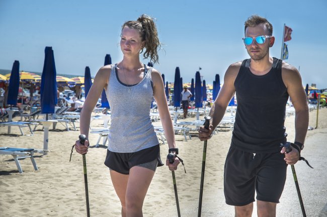 Due persone camminano sulla spiaggia con bastoni da trekking.
