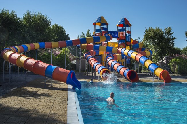 Acquascivoli colorati conducono a una piscina all'aperto con persone che si divertono.