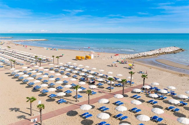 Spiaggia con file di ombrelloni bianchi e blu.