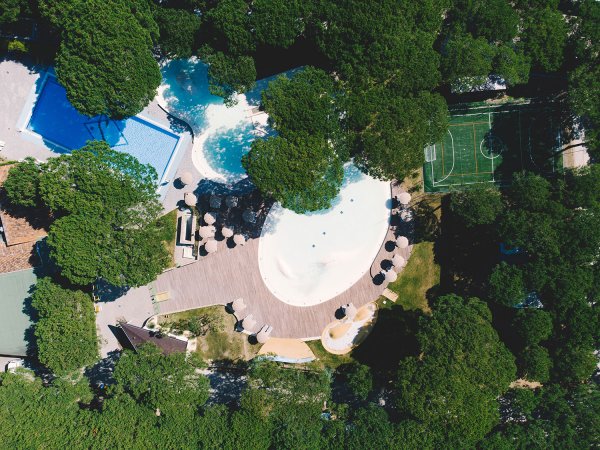 Vista aerea di piscine e campo da calcio tra gli alberi.