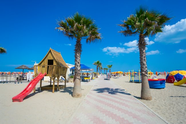 Spiaggia con scivolo rosso e palme.