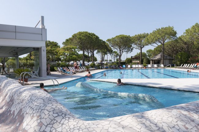 Piscina all'aperto con gente che nuota e prende il sole.