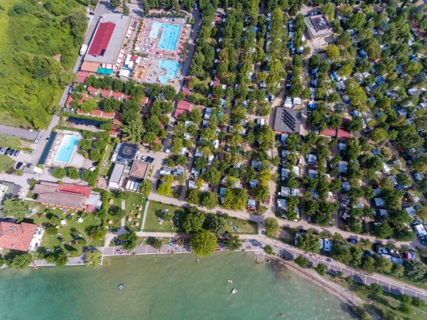 Veduta aerea di un campeggio con piscine e alberi vicino al lago.