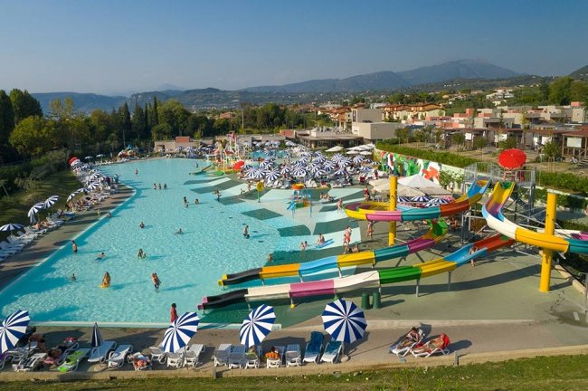 Piscina con scivoli colorati e ombrelloni bianchi e blu.