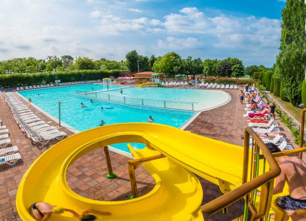 Piscina con scivolo giallo e sedie a sdraio.